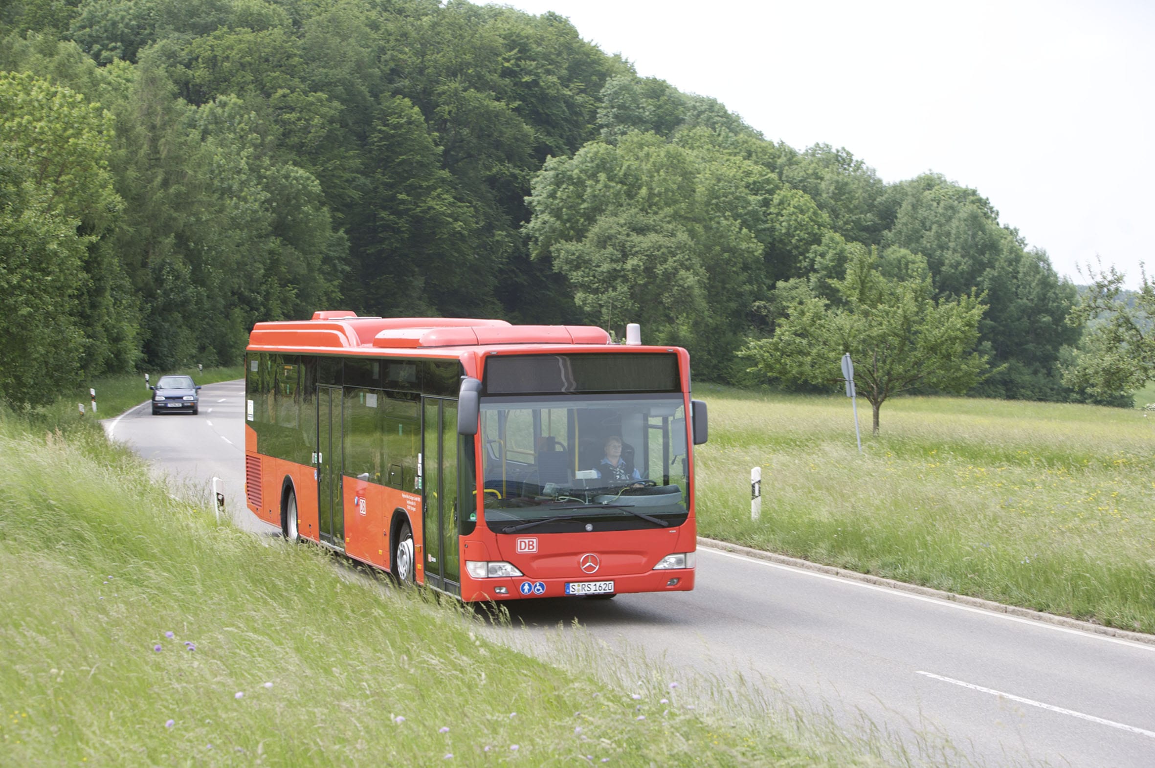Roter Bus auf einer Stra&szlig;e in l&auml;ndlich-gr&uuml;ner Landschaft